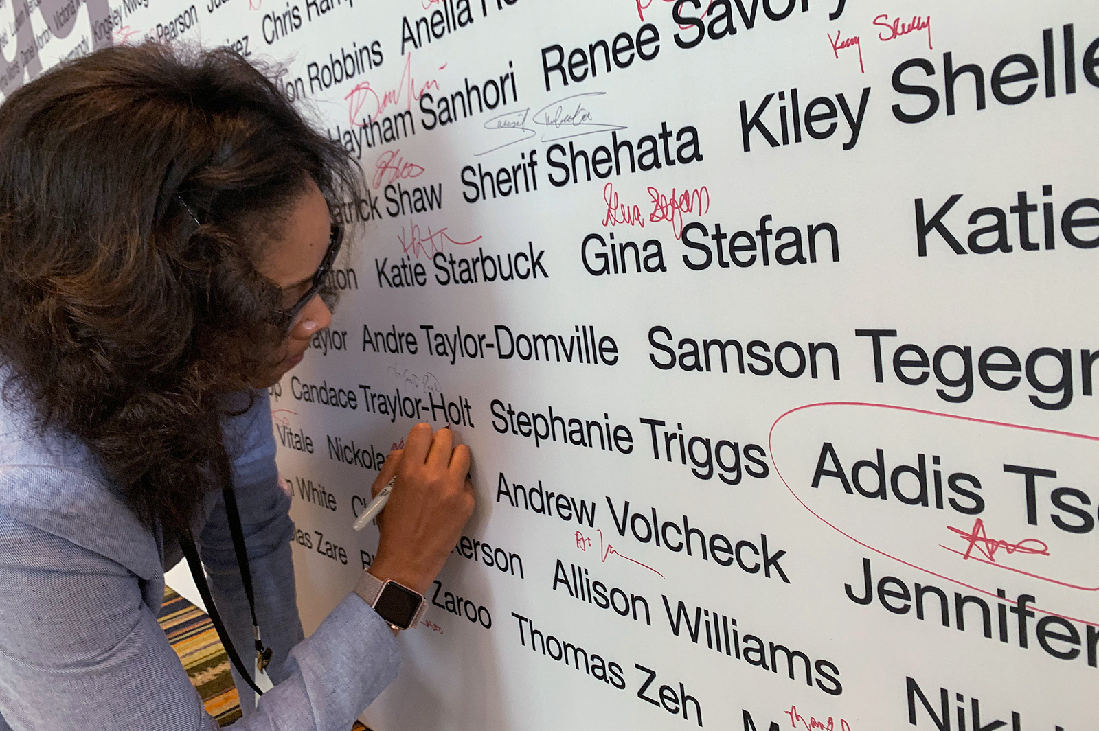 Woman writing her signature on a wall of CVS Paragon Award recipients.